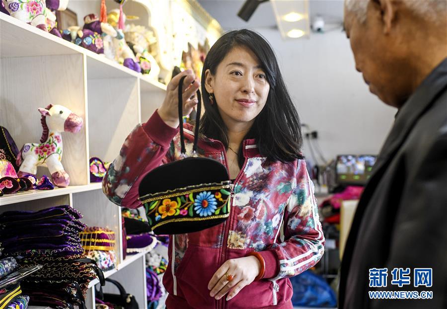 在新疆哈密市一家刺绣手工艺品店内，店主包静（左）向顾客介绍自己设计制作的刺绣工艺品（2019年3月7日摄）。