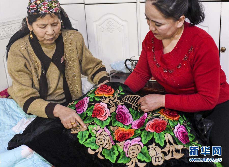 在新疆哈密市，刺绣艺人阿加汗·赛买提（左）和女儿探讨针法（2019年3月6日摄）。